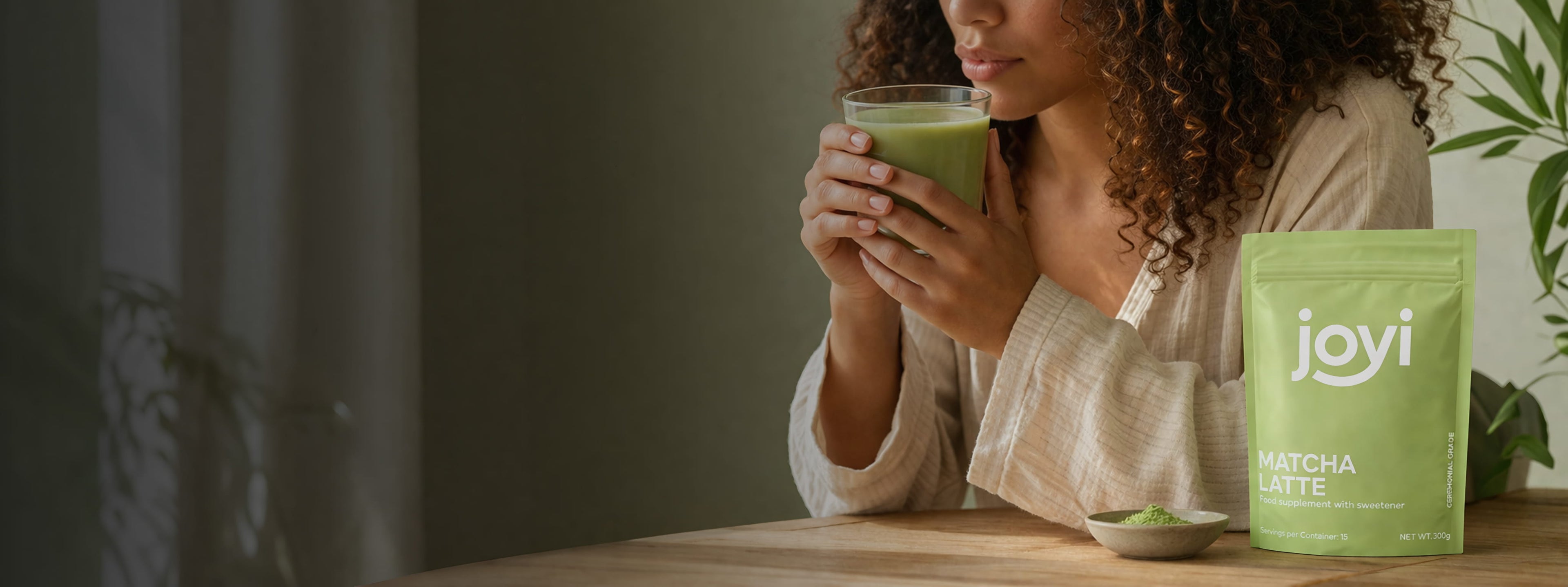 Woman holding a glass of Joyi matcha next to a package of Joyi matcha latte.